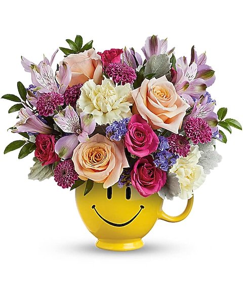 Mixed rose and lilies bouquet with purple accents in a yellow smiley mug from Gurnee flower shop